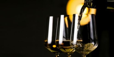 Três copos transparentes com líquido dourado sendo servido num deles, fundo escuro com luz amarela