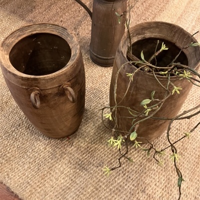 Dois vasos de madeira com planta sobre tapete bege de fibra natural.
