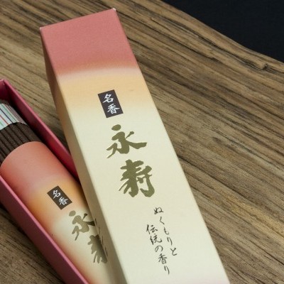 Caixa de incenso rosa e creme aberta com varas coloridas sobre uma mesa de madeira