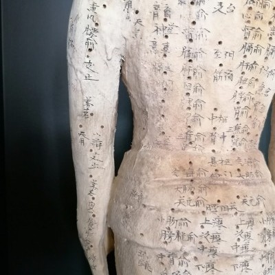 Estátua clara com inscrições em caracteres orientais no tronco e braço esquerdo
