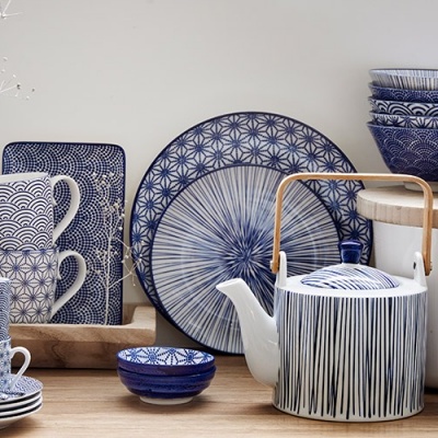 Conjunto de louça azul e branco com padrão distinto e bule com pega de madeira sobre mesa de madeira