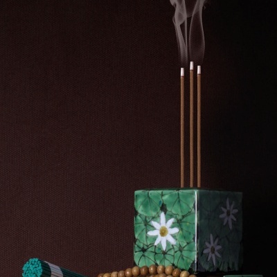 Incensário cúbico verde com flores, paus de incenso queimando, rosário de contas de madeira