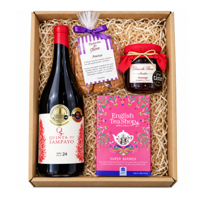 Caixa de presente com vinho tinto, bolachas, doce de morango e chá em embalagem colorida.
