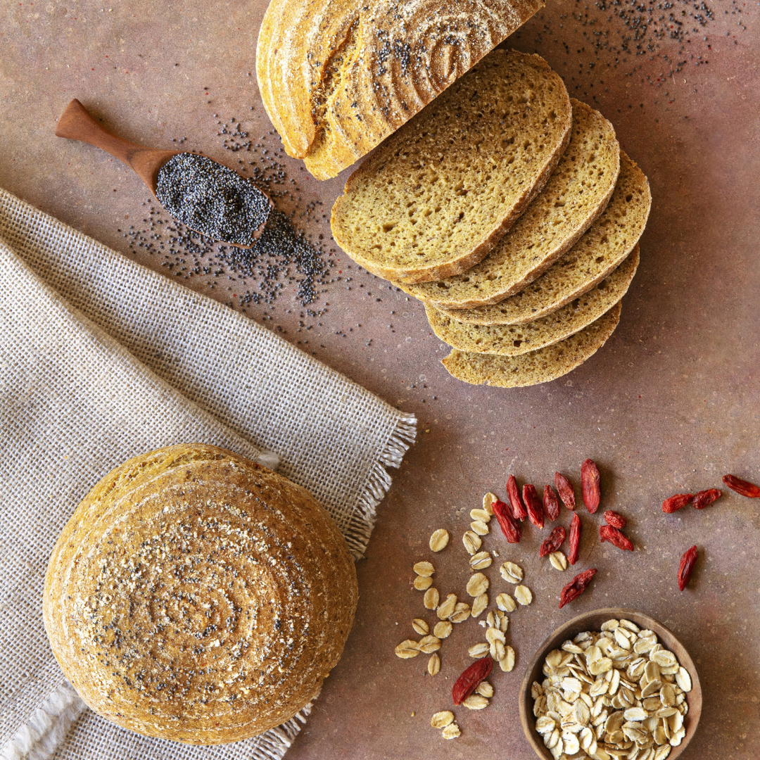 Pão de Aveia e Sementes 300g - Pachamama Pães redondos com sementes, fatiado, sementes de papoila, aveia e frutos vermelhos sobre mesa castanha