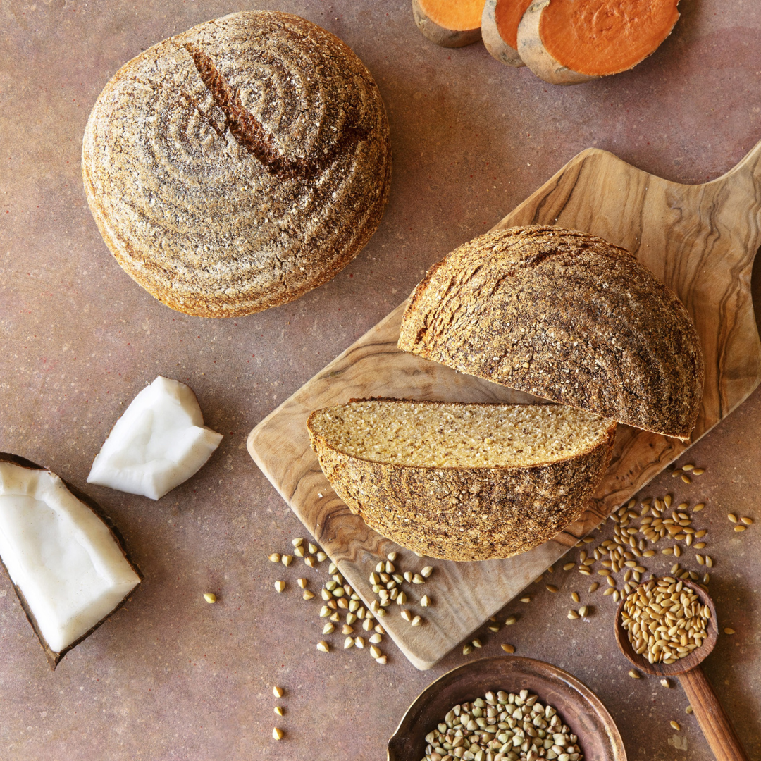 Pão Paleo Low Carb 300g - Pachamama Pão artesanal redondo cortado em fatias com sementes, coco e colher de sementes em tábua de madeira