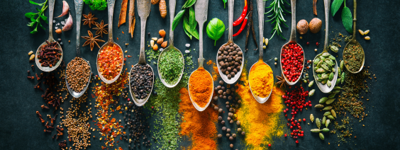 Colheres com especiarias coloridas e ervas frescas em fundo escuro