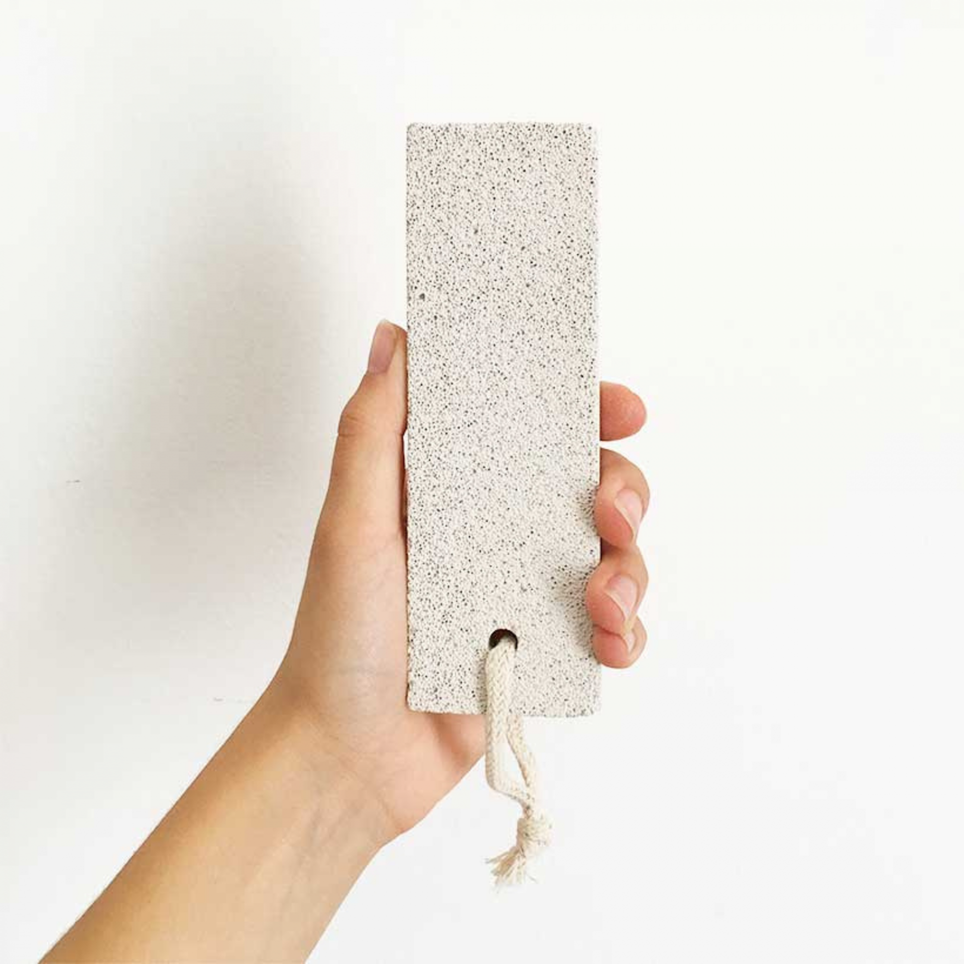 Pedra Pomes Natural - Em Bloco - Croll & Denecke Segurando retângulo claro com textura granular e cordão branco em fundo branco