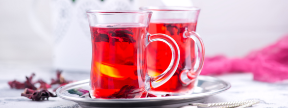 Duas chávenas transparentes com chá vermelho e limão num tabuleiro prateado.