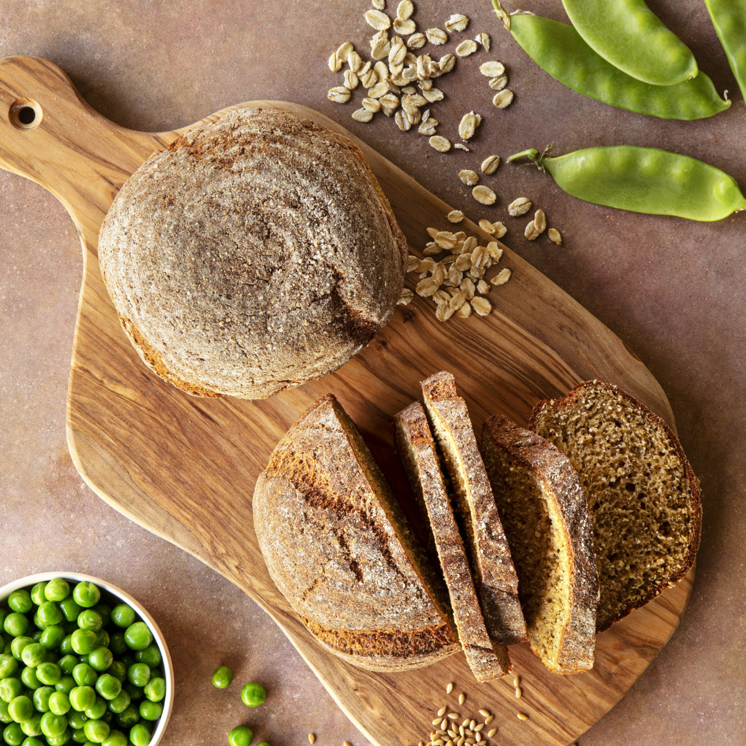 Pão Proteico Low Carb 300g Pachamama Pão integral redondo fatiado em tábua de madeira, com grãos de aveia, vagens e ervilhas verdes