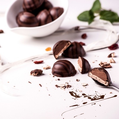 Bombons de chocolate escuro com recheio cremoso em superfície branca com tigela ao fundo