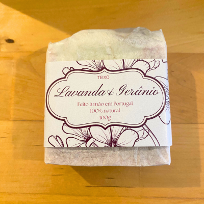 Sabonete Lavanda & Gerânio embalado com etiqueta decorada e texto em português sobre mesa de madeira clara