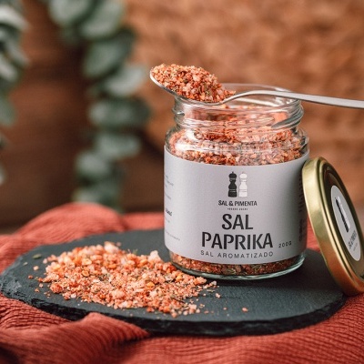 Frasco aberto de sal paprika sobre pedra preta e pano vermelho