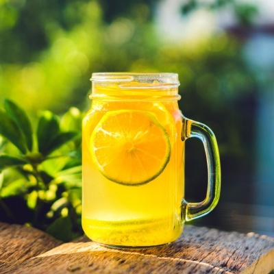 Caneca de vidro com bebida amarela e fatias de limão em superfície de madeira