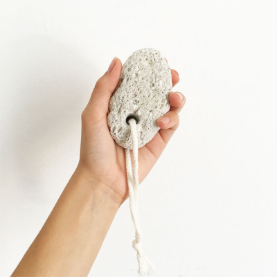 Mão segurando pedra-pomes cinzenta com corda branca em fundo branco