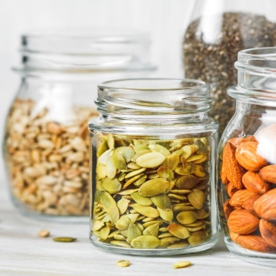 Frascos de vidro com sementes e frutos secos variados em fundo claro