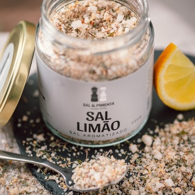 Frasco de sal aromatizado com limão, aberto, com sal visível e uma fatia de limão ao lado