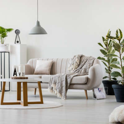 Sala com divã cinzento claro, mesa redonda de madeira, candeeiro pendente e plantas em vasos pretos