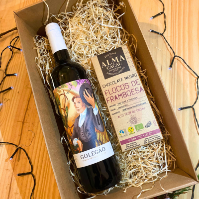 Garrafa de vinho tinto e barra de chocolate numa caixa de presente com enchimento de palha e luzes decorativas