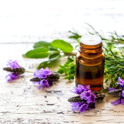 Frasco âmbar com flores de lavanda roxas e folhas verdes sobre mesa branca gasta