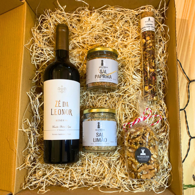 Caixa de presente com vinho, sal aromatizado, tisana e nozes sobre palha.