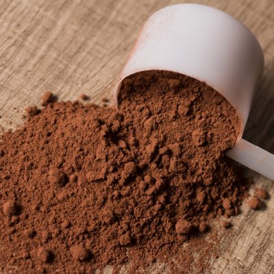 Colher branca com pó castanho escuro sobre madeira clara