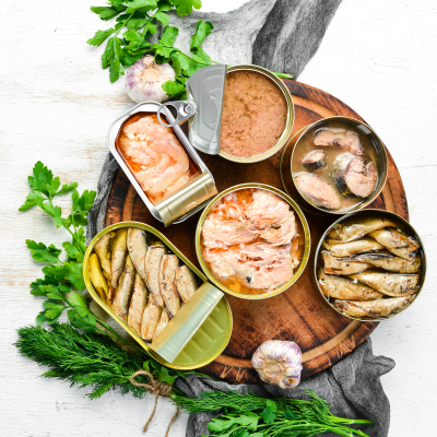 Latas abertas de conservas de peixe variadas num prato de madeira com ervas e alho