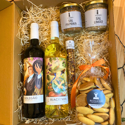Cesto de presente com vinhos, sais aromatizados, tisana e bolachas num fundo de palha dentro de caixa de cartão.