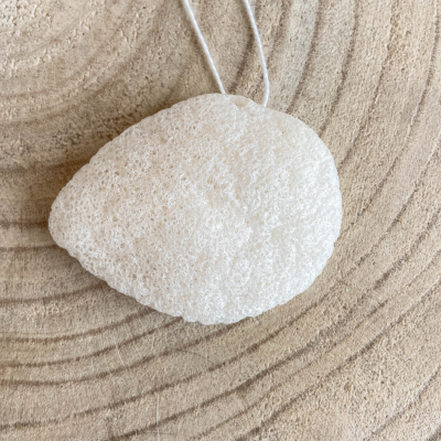 Esponja natural branca com cordão sobre superfície de madeira com anéis concêntricos.