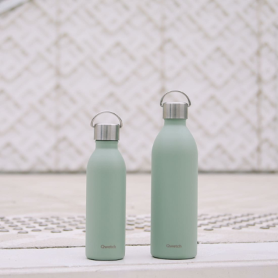 Duas garrafas térmicas verdes pastel com tampas prateadas e alças em cima de superfície branca