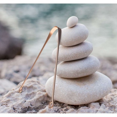 Cinco pedras empilhadas e pinças metálicas douradas sobre rochas junto à água.