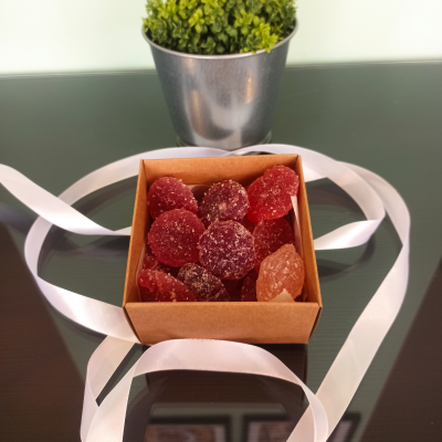 Caixa de gomas vermelhas e alaranjadas em superfície de vidro com fita branca e planta em vaso metálico