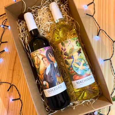 Caixa com duas garrafas de vinho decoradas sobre mesa de madeira com luzes.