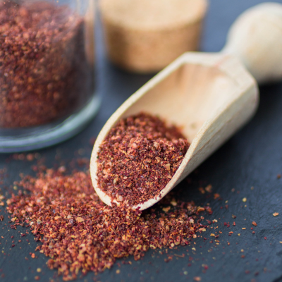 Especiarias moídas castanho avermelhadas numa colher de madeira e frasco de vidro