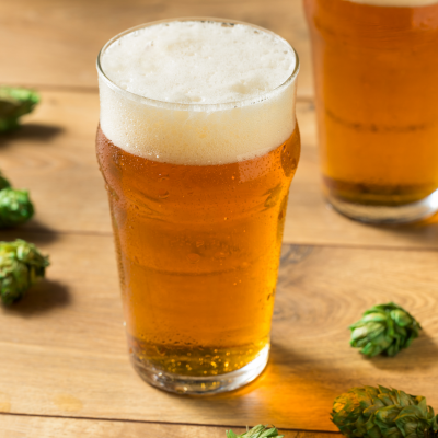 Dois copos de cerveja dourada com espuma sobre mesa de madeira com lúpulo verde