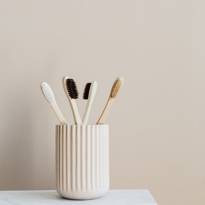 Escovas de dentes de madeira num copo creme texturizado sobre superfície branca