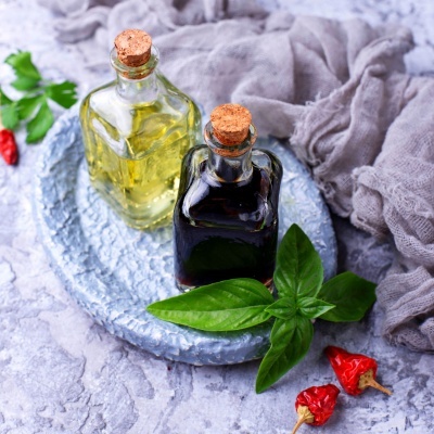 Duas garrafas de vidro com líquidos amarelo e escuro, folhas verdes e pimentos vermelhos em fundo cinza