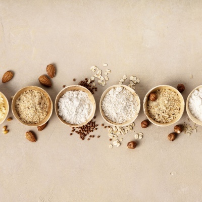 Seis tigelas de madeira com farinhas e frutos secos sobre superfície bege