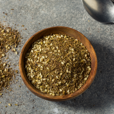 Taça de madeira com tempero seco e sementes sobre superfície cinza, colher metálica ao lado