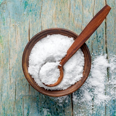 Taça de madeira com sal grosso branco e colher de pau numa mesa de madeira azul desgastada