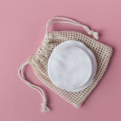 Discos de algodão reutilizáveis brancos sobre saco de rede em fundo rosa