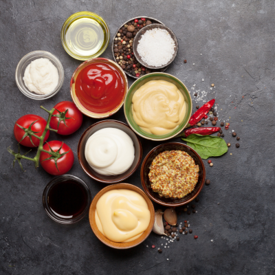 Vários molhos e condimentos em recipientes redondos com tomates e especiarias num fundo cinzento