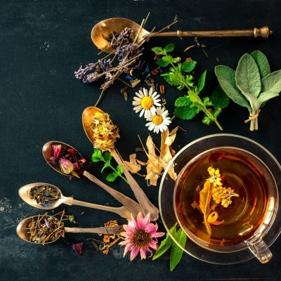 Chávena de chá com ervas e flores secas em colheres douradas sobre superfície escura