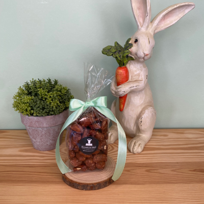 Saco de amêndoas cobertas com laço verde, ao lado de planta e figura de coelho segurando cenoura