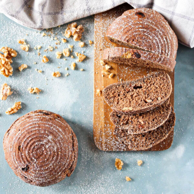Pão escuro com nozes fatiado sobre tábua de madeira com farinha e nozes ao redor