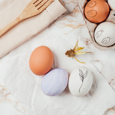 Ovos decorativos com desenhos, espátula de madeira e embalagem de cartão sobre superfície de mármore