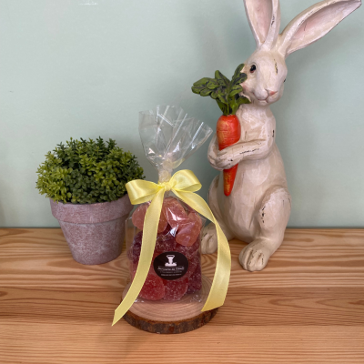 Saco de gomas vermelhas com fita amarela ao lado de vaso com planta e estátua de coelho segurando cenoura