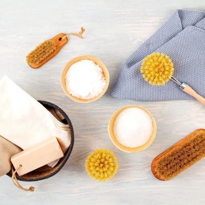 Acessórios de limpeza doméstica com escovas, tigelas e panos sobre superfície clara