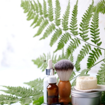 Produtos de cuidados pessoais com frascos, pincel e esponja sobre folhas verdes