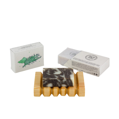 Sabonete vegetal marmoreado preto e branco em suporte de madeira com embalagem branca com texto e ilustração de planta.