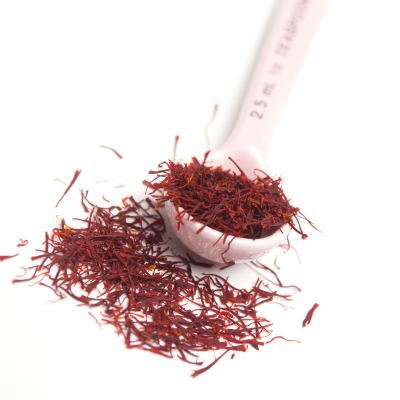 Fios de açafrão numa colher medidora rosa sobre fundo branco
